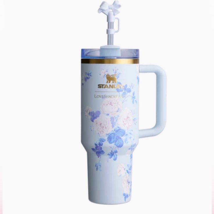 a white and blue flowered travel mug with handle on the side, in front of a white background