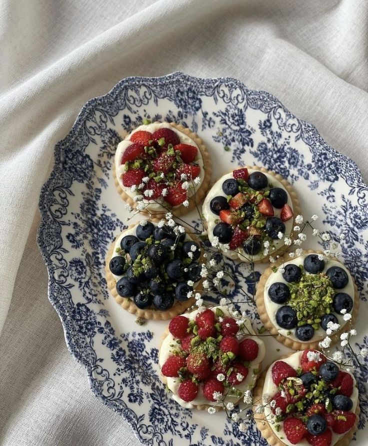 small desserts on a blue and white plate topped with strawberries, blueberries, raspberries, and pistachio