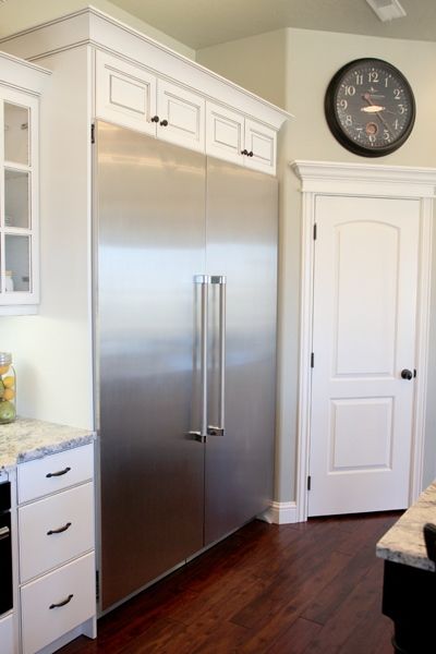 a kitchen with white cabinets and stainless steel refrigerator freezer next to a clock on the wall