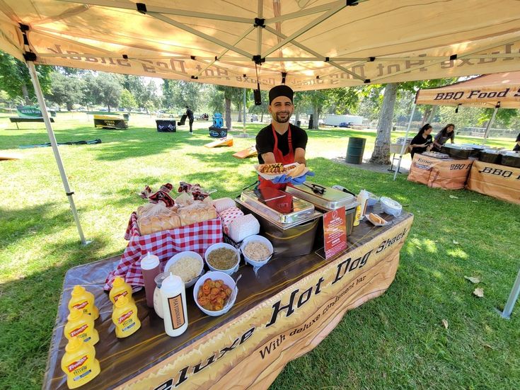 a woman standing at a table with food on it in the grass under a tent