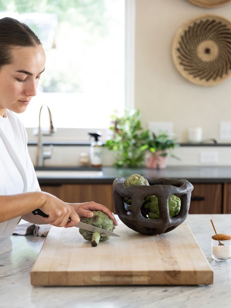 a woman cutting broccoli on top of a wooden cutting board in a kitchen