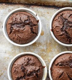 four chocolate cupcakes in white bowls on a baking sheet