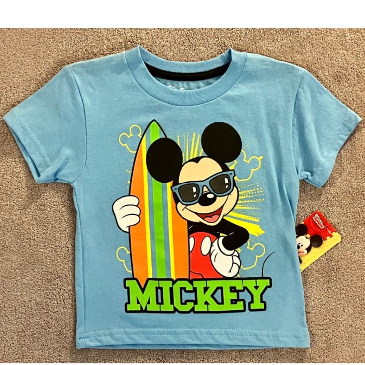 This Fun Disney Mickey Mouse T-Shirt Is Perfect For Little Beach Lovers! Available In Many Sizes, It Features A Cute Surfing Beach Theme That Any Toddler Boy Will Love. Made With Quality Materials And Featuring The Beloved Disney Character, This T-Shirt Is Sure To Become A Favorite. Playful Cartoon Print T-shirt For Disney Trips, Disney Summer Cartoon Print T-shirt, Themed Short Sleeve Tops For Disney Trips, Disney Character Print Summer T-shirt, Blue Character Print T-shirt For Summer, Disney Crew Neck T-shirt For Summer, Mickey Mouse Themed Cotton Top, Themed Mickey Mouse Cotton Top, Themed Mickey Mouse Short Sleeve T-shirt