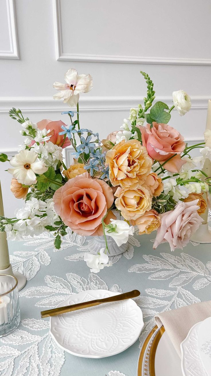 an arrangement of flowers in a glass vase on a table with plates and napkins