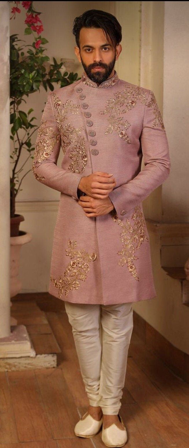 a man in a pink sherwa with white pants and shoes standing next to a potted plant