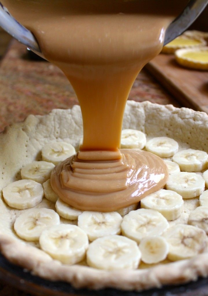 a person pouring peanut butter on bananas in a pie pan