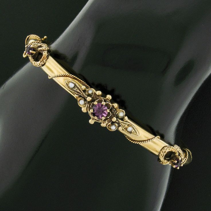 "This fine antique bangle bracelet was crafted from solid 14k yellow gold during the Victorian era. It features 3 old round cut purple stones neatly prong set across its top with the center stone being slightly larger. All three of the stones display a truly gorgeous and well matched deep purple color with lovely shine that brings such an attractive and rich look to this piece. It is further adorned with 6 adorable cultured seed pearls neatly set throughout the center design for a wonderful touc Victorian Gold Bangle Bracelet With Intricate Design, Antique 14k Gold Bracelet With Intricate Design, Victorian Yellow Gold Bangle Bracelet, Victorian Style Yellow Gold Bangle Bracelet, Victorian Bangle With Intricate Design For Anniversary, Antique 14k Gold Bangle Bracelet, Antique 14k Gold Bracelet For Anniversary, Victorian Gold Bracelet For Anniversary, Antique Stamped 14k Bangle Bracelet