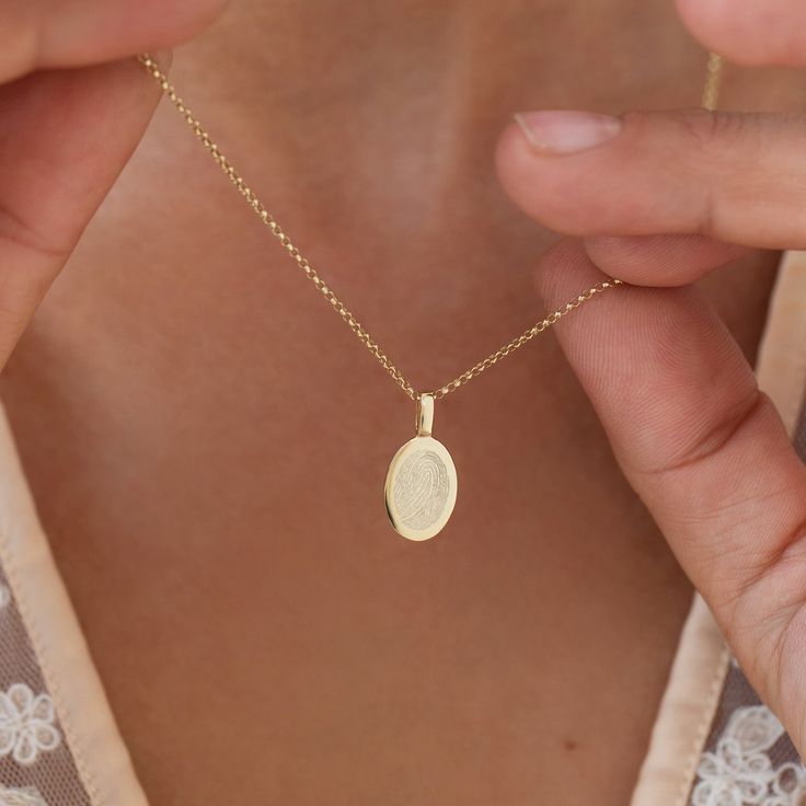 "Introducing our exclusive Personalised Oval Charm Necklace, a stunning piece of jewellery that holds a truly special meaning. Crafted with utmost care and precision, this necklace features an oval charm that can be imprinted with the unique fingerprint of your loved one. It's a beautiful way to keep them close to your heart wherever you go. To make this necklace even more personal, you can also have the reverse side of the charm personalised with a name or a significant date. Whether it's a beloved family member, a dear friend, or a soulmate, this necklace serves as a touching tribute to the special bond you share. The charm is expertly crafted in 9ct Gold, adding an elegant touch to its overall appeal. It hangs delicately from a fine chain, creating a graceful and refined look. Presented Personalized Oval Yellow Gold Charm Necklace, Oval Yellow Gold Locket Necklace With Engraving Option, Dainty Oval Necklaces For Keepsake, Yellow Gold Charm Necklace With Oval Pendant, Dainty Engraved Oval Charm Necklaces, Dainty Oval Engraved Charm Necklaces, Dainty Engraved Oval Charm Necklace, Yellow Gold Oval Charm Necklace As Gift, Yellow Gold Oval Charm Necklace Gift