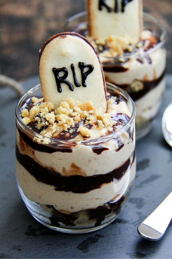 two desserts with halloween decorations in them on top of a slate board next to spoons