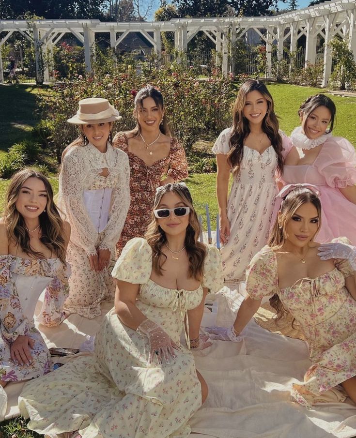 a group of women in dresses and hats posing for a photo on a blanket outside