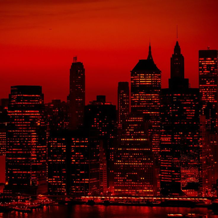 the city skyline is lit up at night with red light in the sky and water