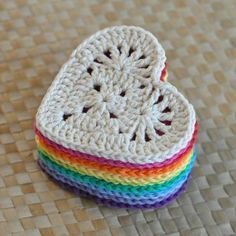 two crocheted hearts sitting on top of a woven tablecloth covered in multicolored yarn