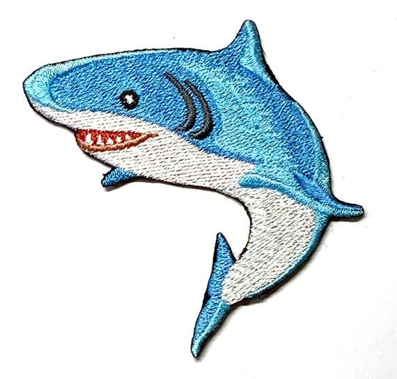 a blue and white shark with teeth on it's back, embroidered onto a white surface