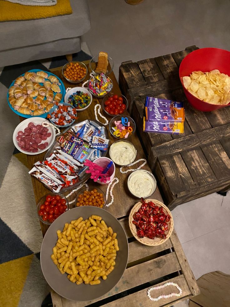 a table filled with snacks and candy on top of wooden pallets next to a red bowl