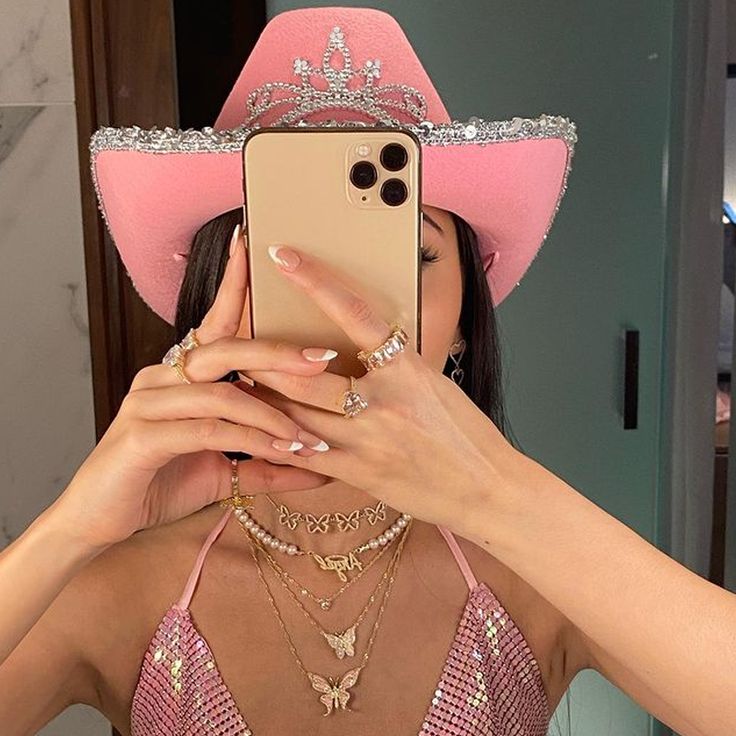 a woman taking a selfie with her cell phone wearing a pink hat and necklaces