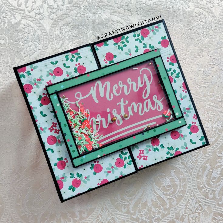 a close up of a christmas card on a white surface with pink and green flowers