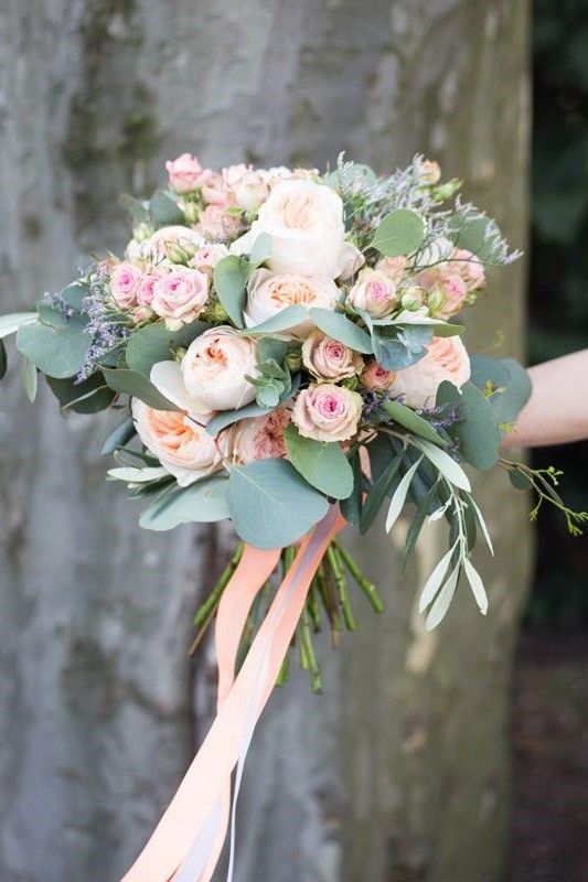 a bridal bouquet with pink roses and greenery is held by someone's hand