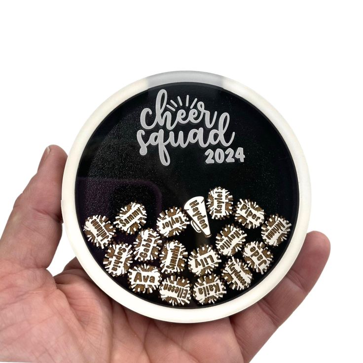 a hand holding a black and white badge with words on it that say cheer squad