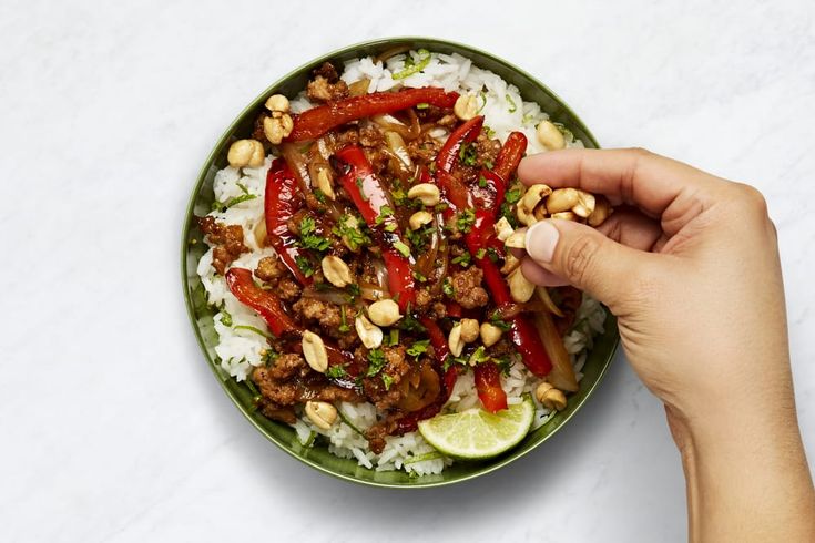 a person holding a plate with rice, meat and peppers on it next to chopsticks