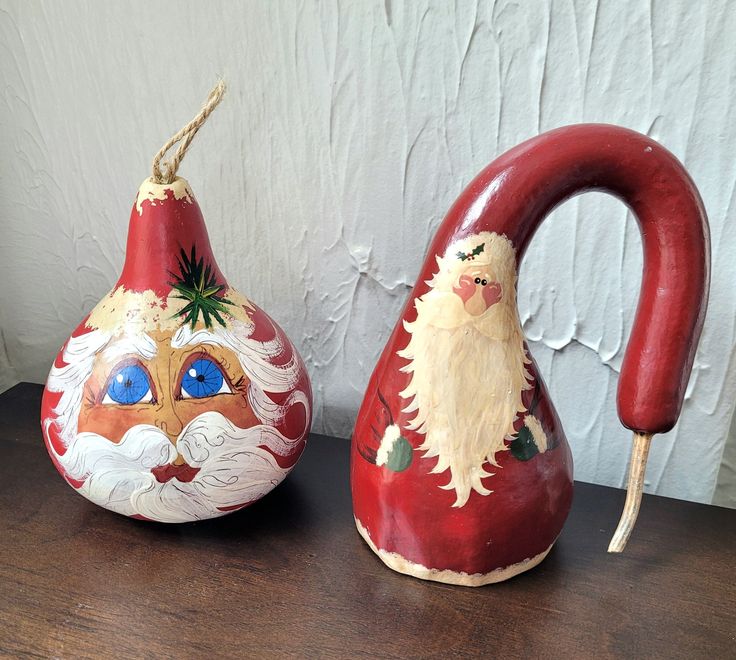 two red vases with santa claus faces on them sitting on a wooden table next to a white wall