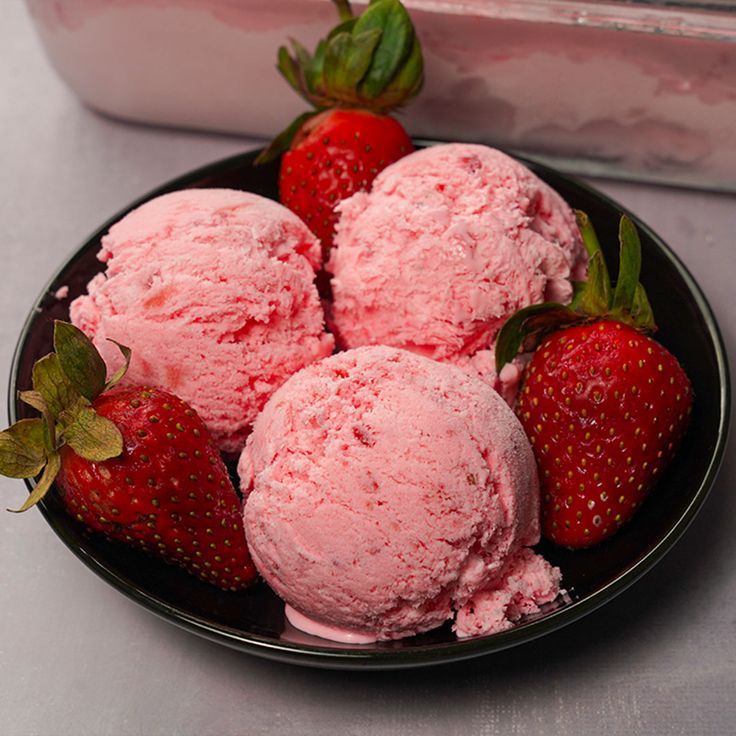 three scoops of ice cream with strawberries on a plate next to a container