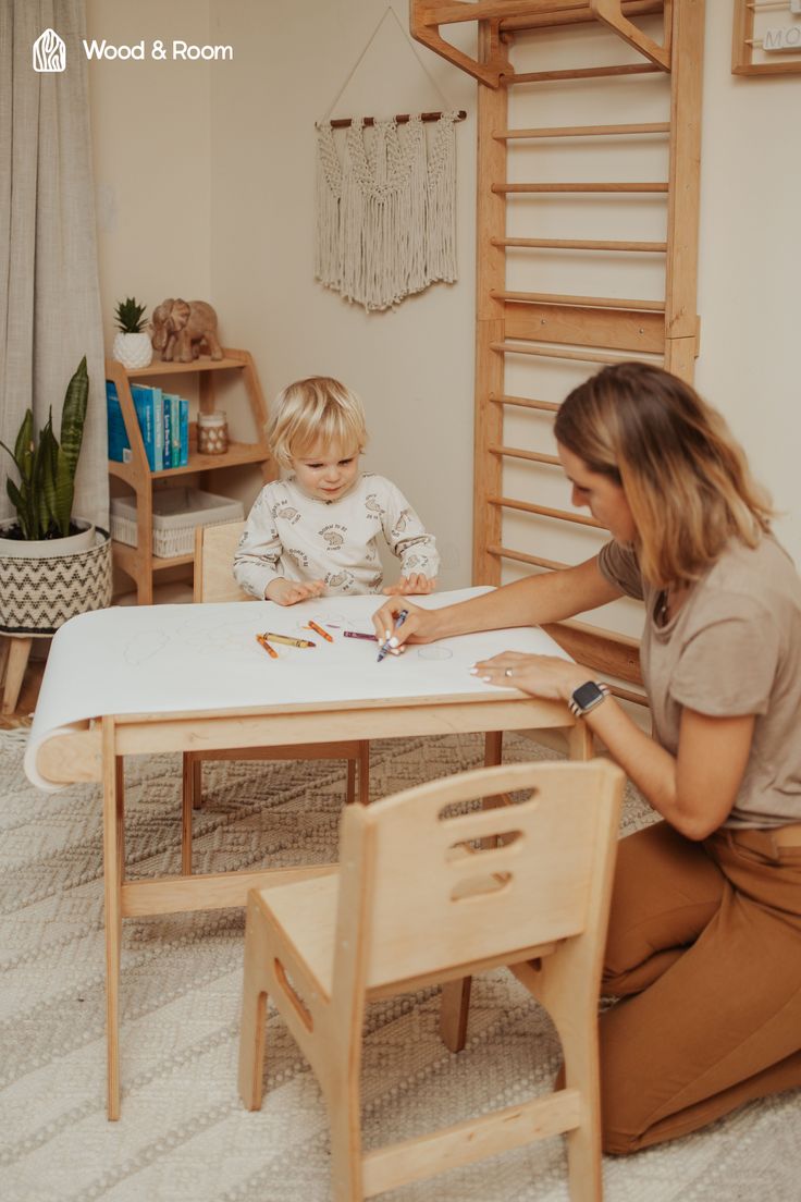 a woman sitting at a table with a child in front of her and crayons on the table