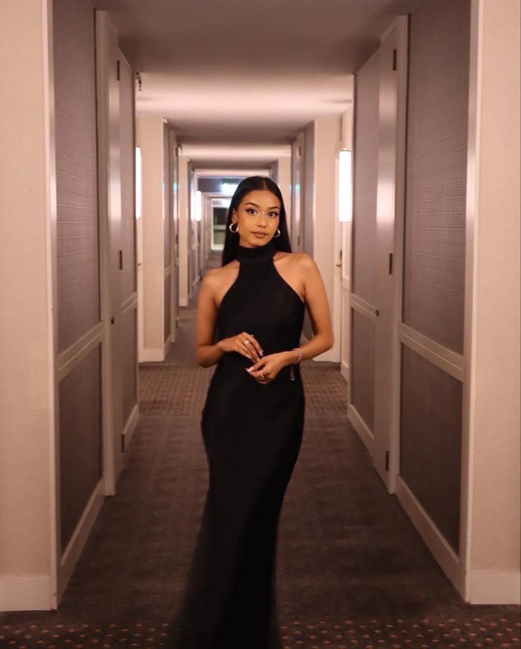 a woman in a long black dress is standing in an empty hallway with her hands on her hips