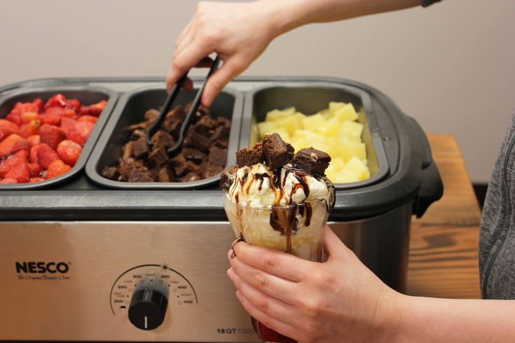 a person holding an ice cream sundae in front of a toaster with strawberries and other desserts