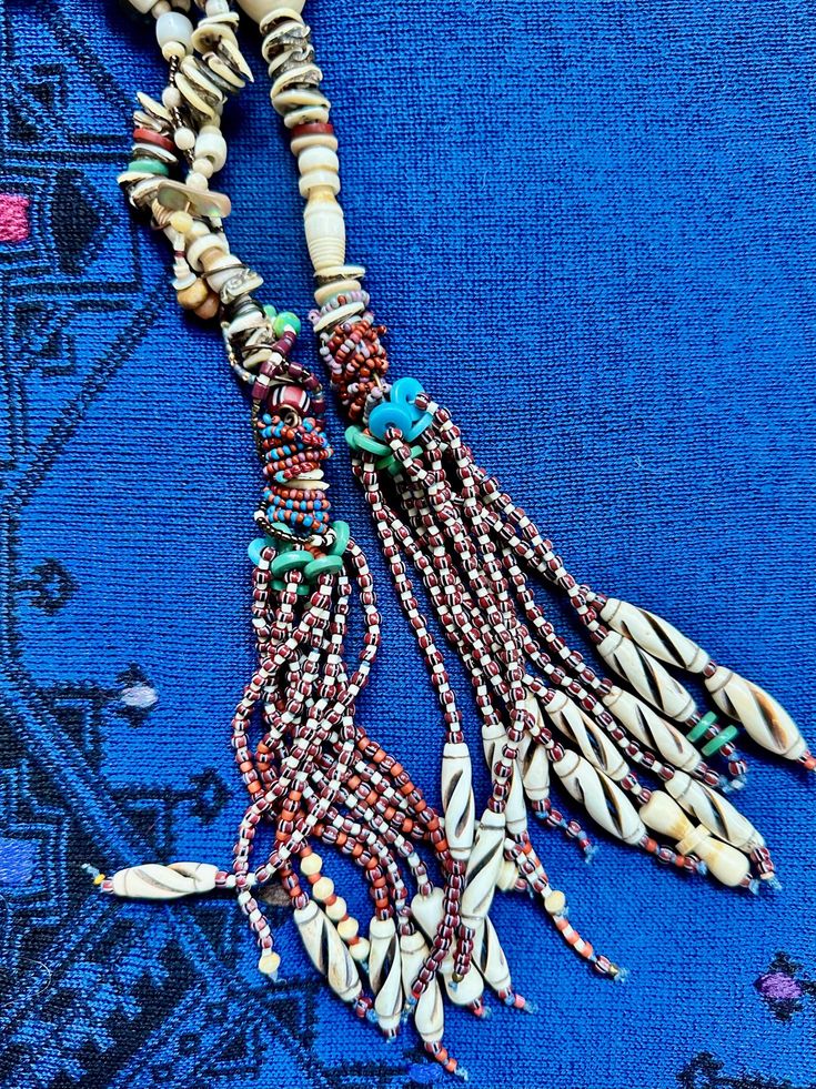 This unique design employs an eclectic array of beads. The beauty is in the details: neutral shades of sand and beach washed shell contrasted with tassels of glass seed beads. The tassels are earthy reds accented by faded aqua and turquoise glass beads. The bead materials include new and old shell and shell beads, bone, glass, and large vintage Lucite beads. The latter are visually pleasing, upcycled and serve a structural purpose without contributing additional weight. Bohemian Hand-strung Beaded Necklaces For Beach, Beach Jewelry With Brown Tassels, Traditional Hand-strung Beads For Beach, Handmade Bohemian Sand-colored Jewelry, Bohemian Multi-strand Dangling Beads, Bohemian Beaded Necklace With Large Beige Beads, Bohemian Beige Beaded Necklace With Large Beads, Bohemian Brown Lariat Beaded Necklaces, Bohemian Hand-strung Lariat Beaded Necklace