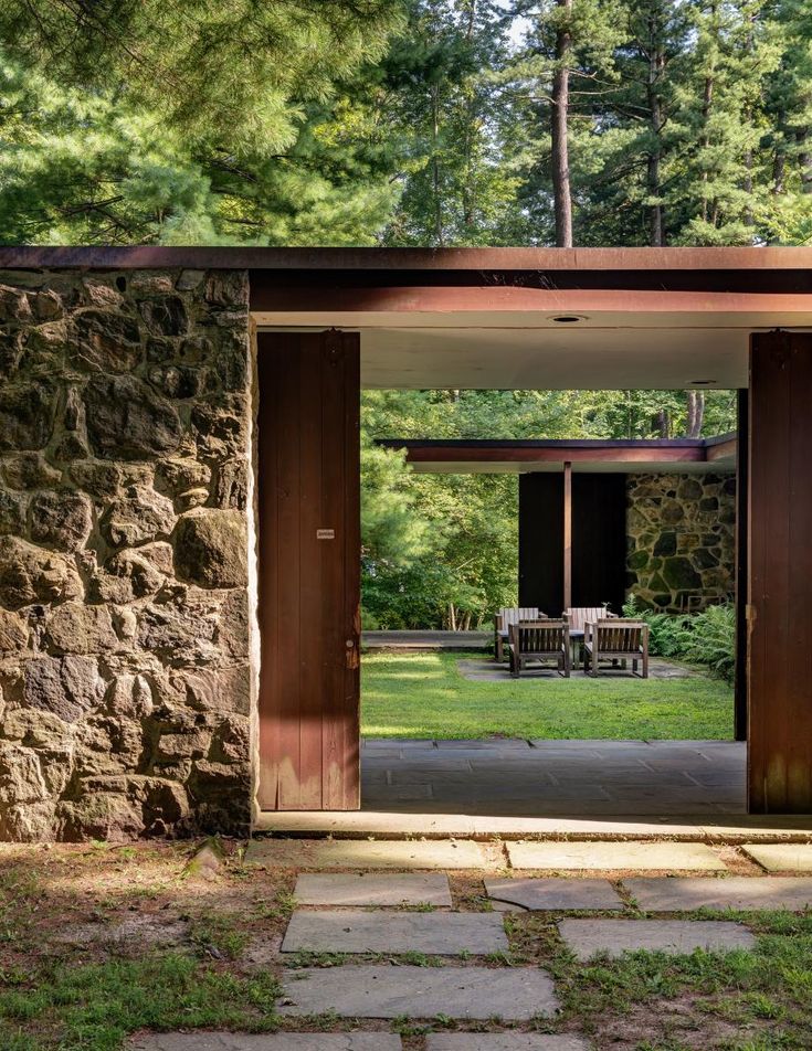 an open door to a stone building with picnic tables in the back ground and trees behind it