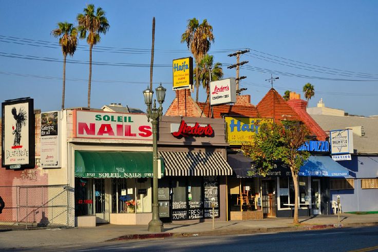 an empty street with shops and palm trees on the side walk in front of it