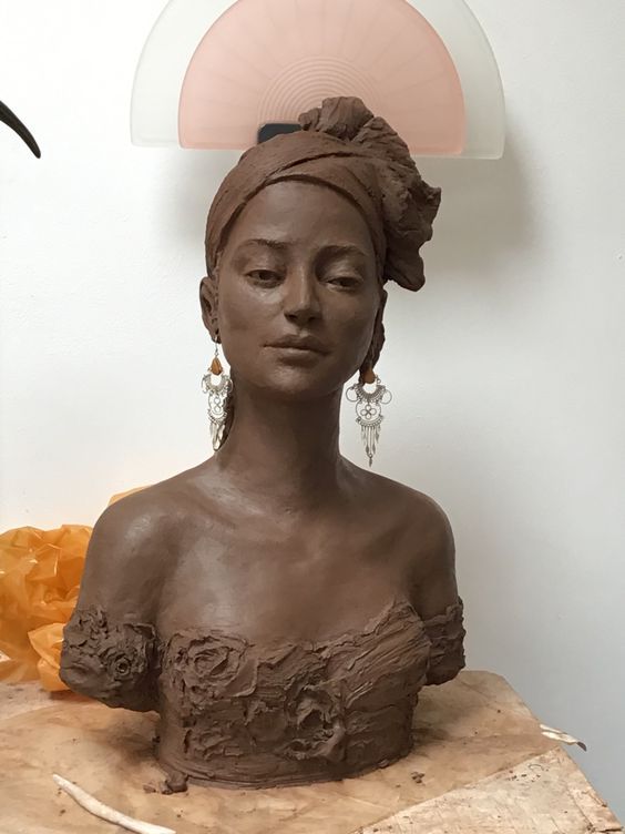 a clay sculpture of a woman's head with her eyes closed on a piece of wood