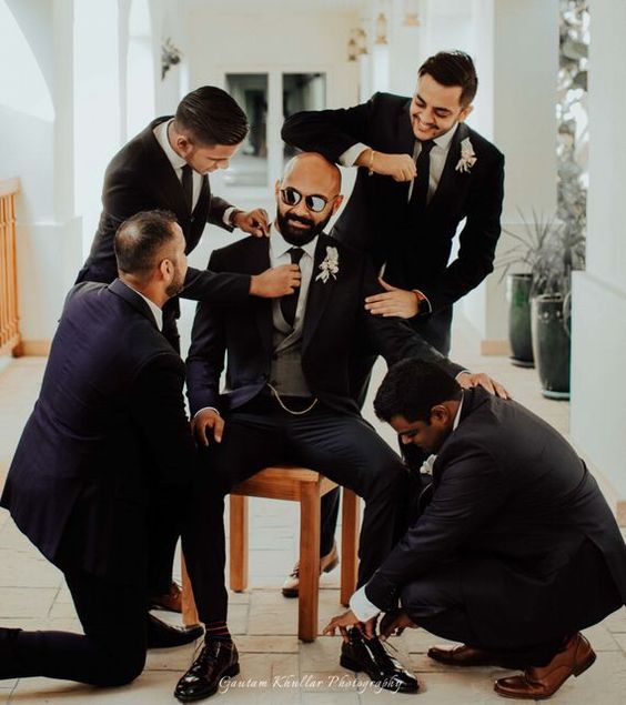 a group of men in suits and ties sitting on a chair with one man adjusting his tie