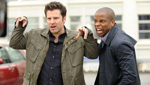 two men standing next to each other in front of a red car, one pointing at the camera