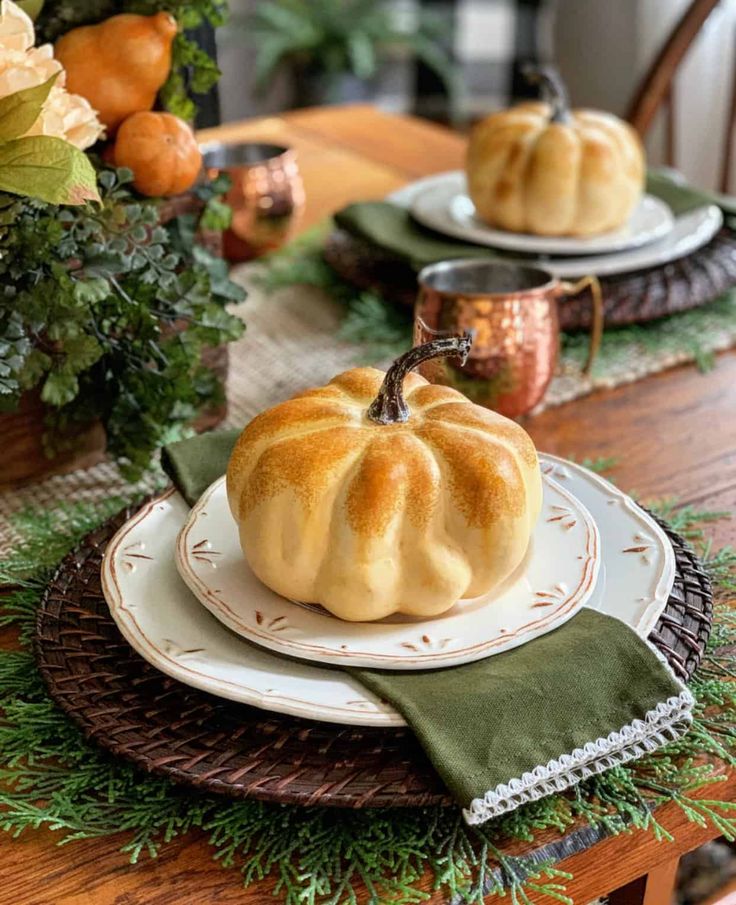 a table set for thanksgiving with pumpkins and greenery on the placemats