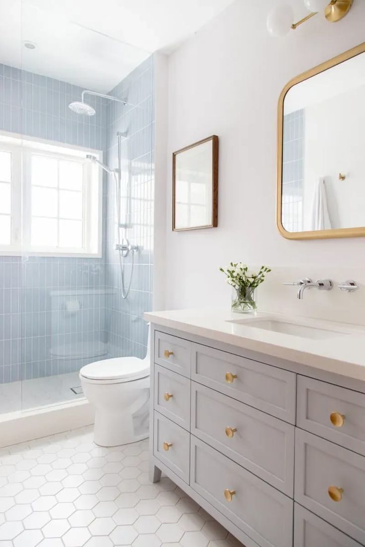 a white bathroom with blue tile and gold accents on the vanity, toilet and shower