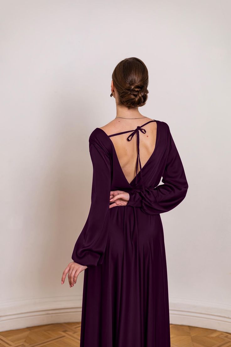 the back of a woman wearing a purple dress with long sleeves and tie at the neck