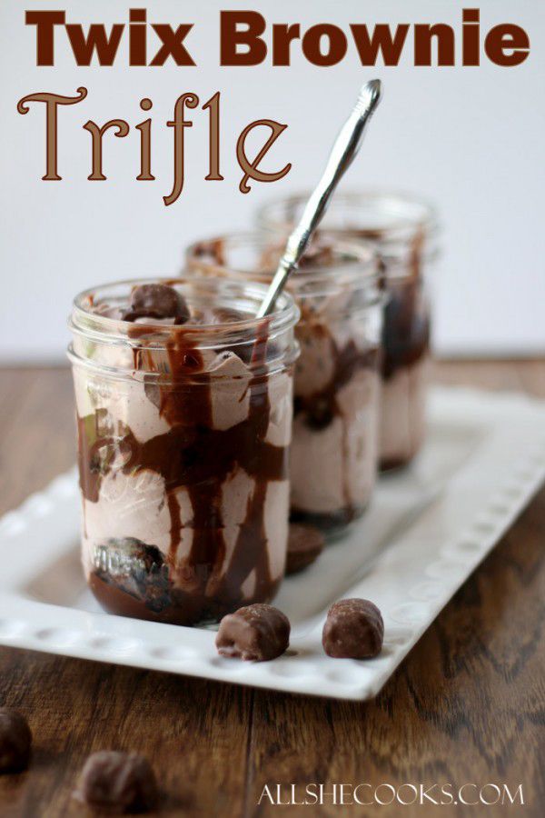 chocolate brownie trifle in a glass jar with spoon on white serving tray and text overlay that reads, twix brownie trifle