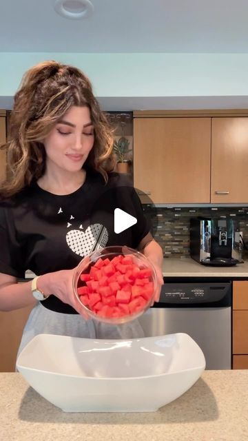 a woman is holding a bowl full of red candy canes while standing in the kitchen