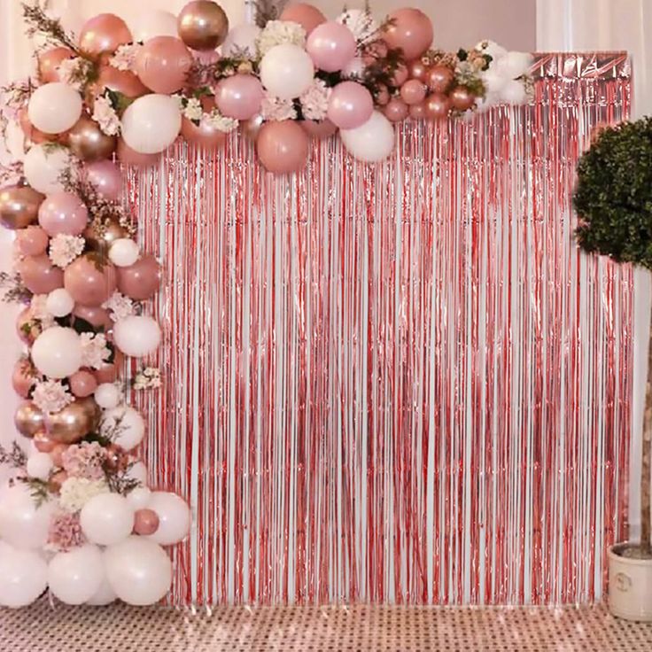 a pink and white backdrop with balloons, flowers and streamers on the wall in front of it