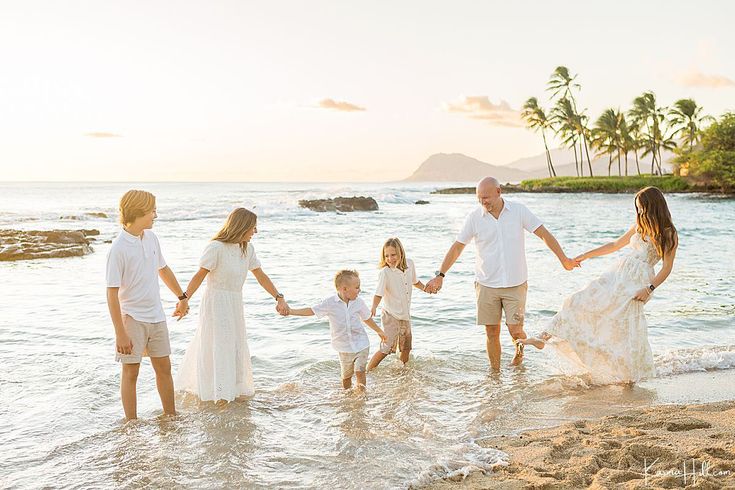 a family holding hands and walking into the water at sunset on a beach with palm trees in the background