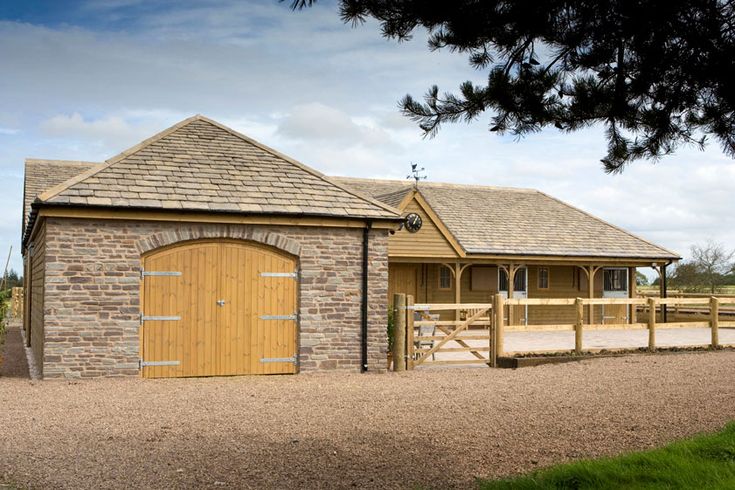 a horse barn with a wooden gate and brown brick building next to it on a dirt road