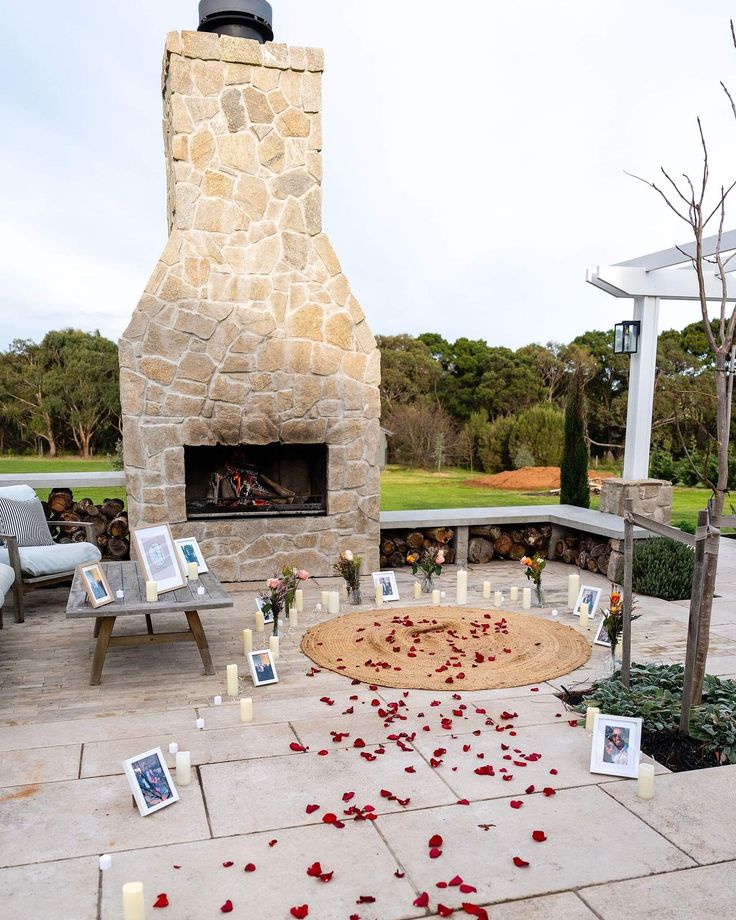 a fire place with rose petals on the ground and pictures around it, surrounded by chairs