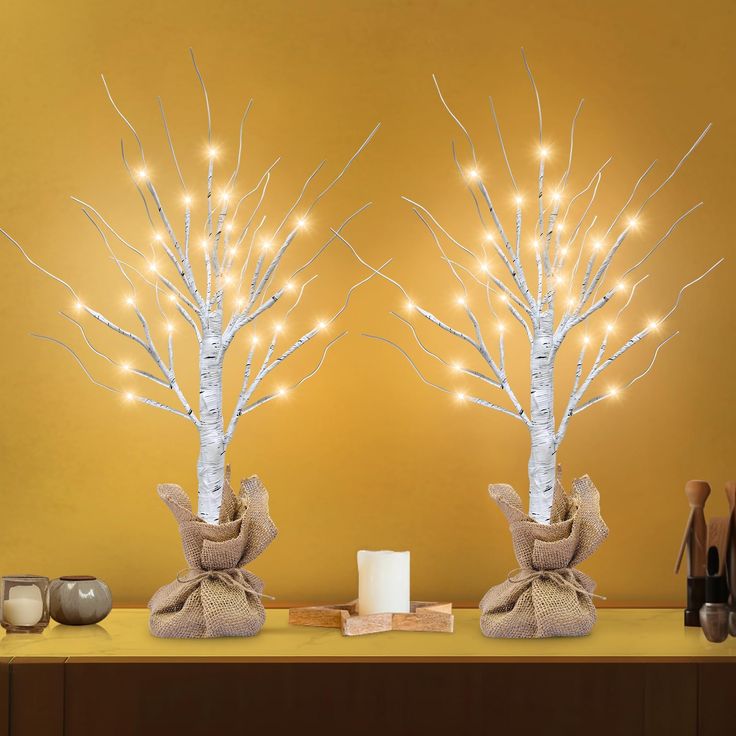 two white trees decorated with lights on a table