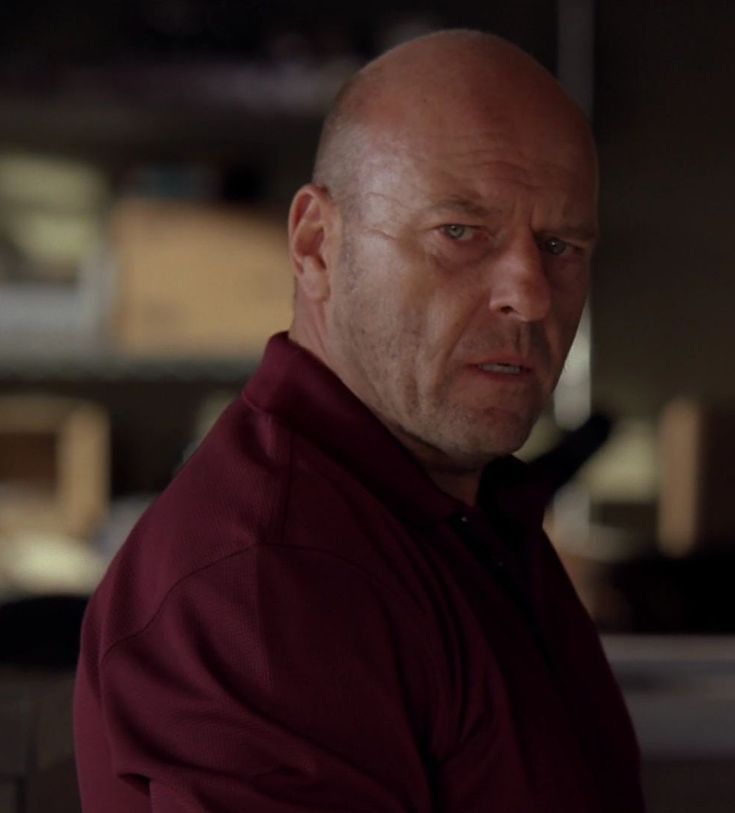 a bald man in a red shirt looking at the camera with an intense look on his face