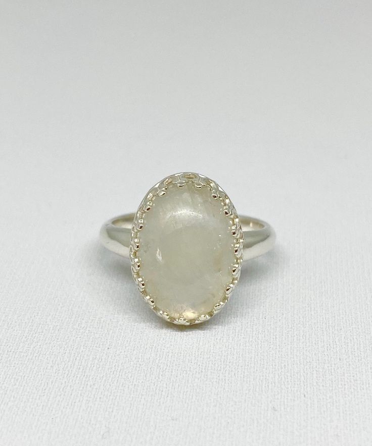 This cool, white Rainbow Moonstone gemstone ring reminds me of the puffy clouds that accent a Spring day. After a rain you can see the dark clouds turn to wisps of white with a faint rainbow glistening through. This stone is just that! As you look at the ring and turn it you will see subtle flashes of blue purple and maybe green. The lovely way the stone is nestled within the Sterling silver scalloped bezel setting gives this special piece a dainty yet bold look and feel. Designed in a timeless Celestial White Moonstone Birthstone Ring, Celestial White Moonstone Ring As Birthstone, Celestial Style White Moonstone Birthstone Ring, Celestial White Promise Ring Jewelry, White Celestial Jewelry For Promise Ring, Celestial White Moonstone Ring With Halo, Celestial Style White Moonstone Ring With Halo, White Moon-shaped Birthstone Rings, White Moon Shaped Ring With Birthstone