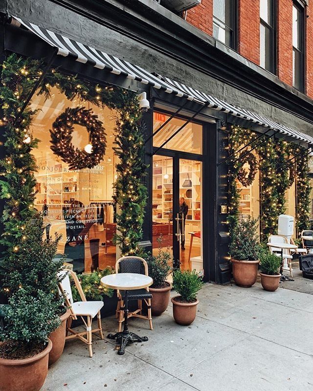 a store front with potted plants and christmas wreaths on the windows, along with chairs and tables