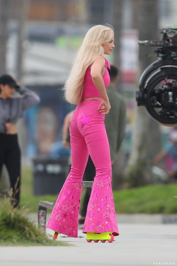 a woman with blonde hair wearing pink pants and high heels is standing on the sidewalk