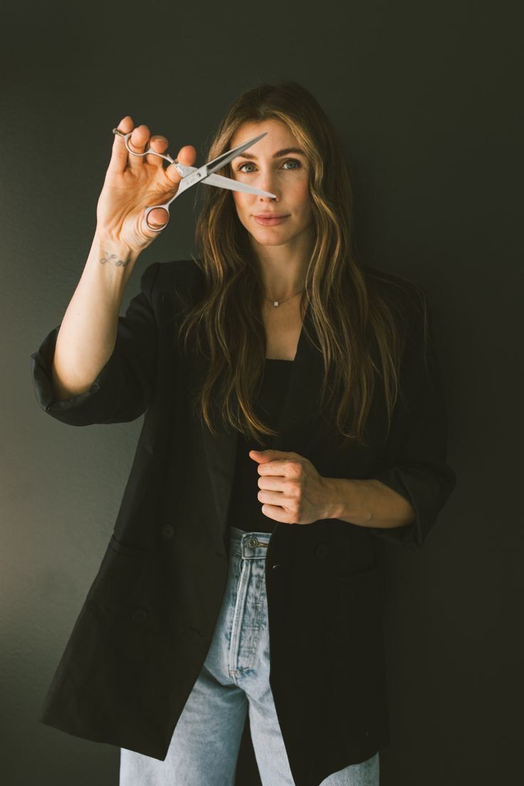 a woman holding scissors up to her face and looking at the camera while standing in front of a black wall