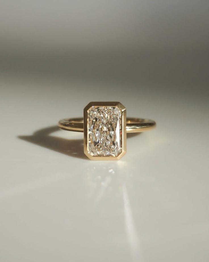 a yellow gold ring with a square cut diamond in the center on a white surface